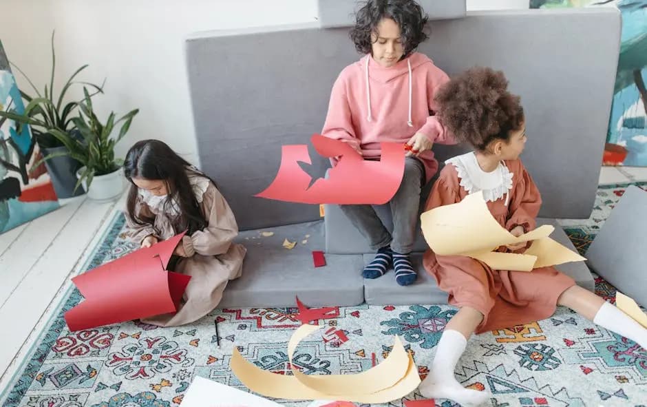 Three children sitting indoors, cutting colorful paper for a school art project.